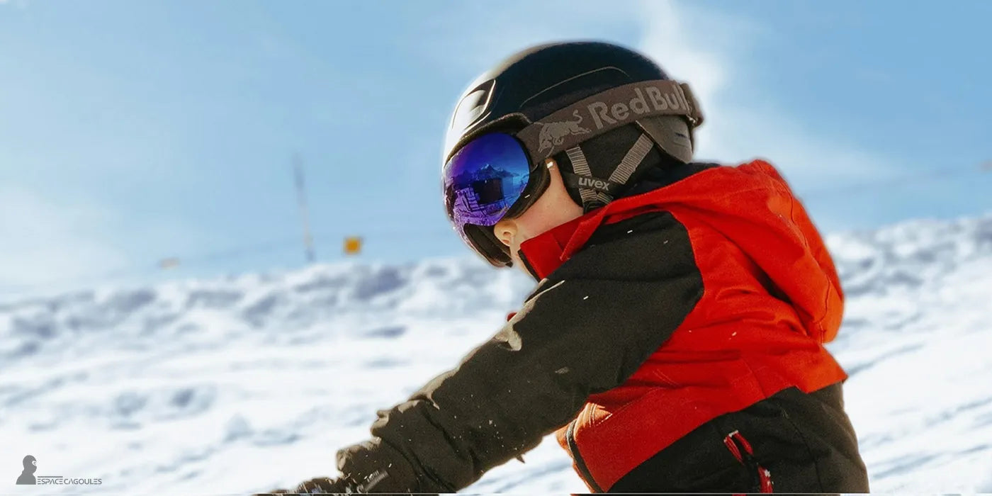 Cagoule ski enfant blanche portée sous un casque noir et masque de ski miroir, enfant en veste rouge jouant dans la neige sous un ciel bleu – Espace Cagoules