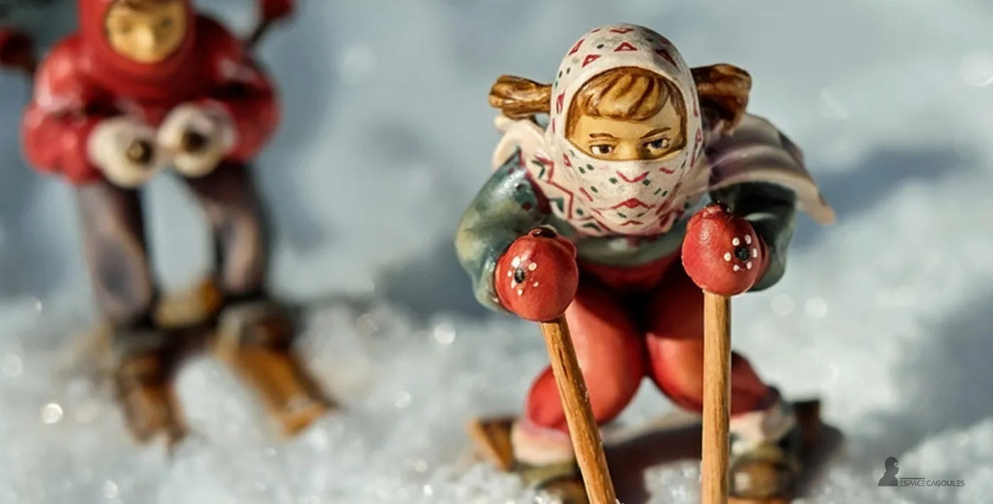 Cagoule ski enfant sur petite figurine d’enfant en tenue de ski rouge et verte avec cagoule imprimée, dévalant une pente enneigée miniature – Espace Cagoules