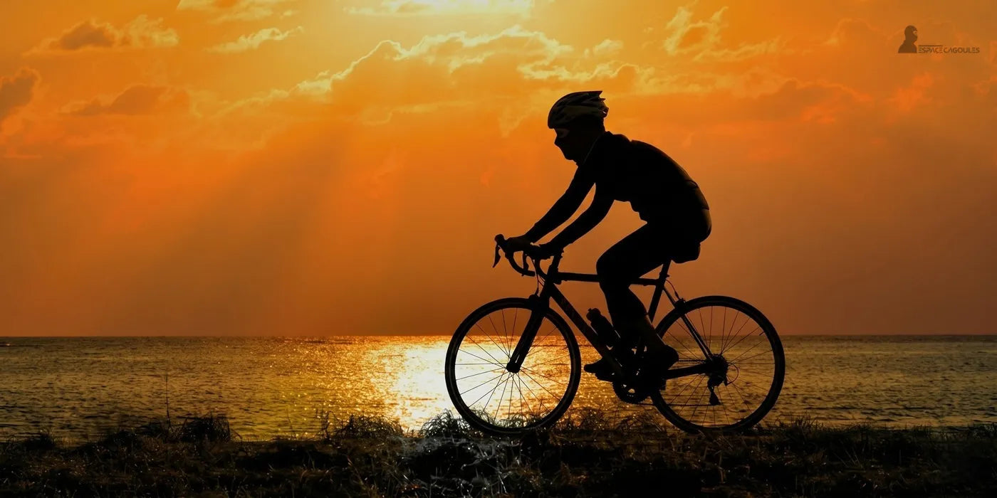 Cycliste portant une cagoule légère roulant en bord de mer au coucher du soleil avec casque et vélo de route - Espace Cagoules