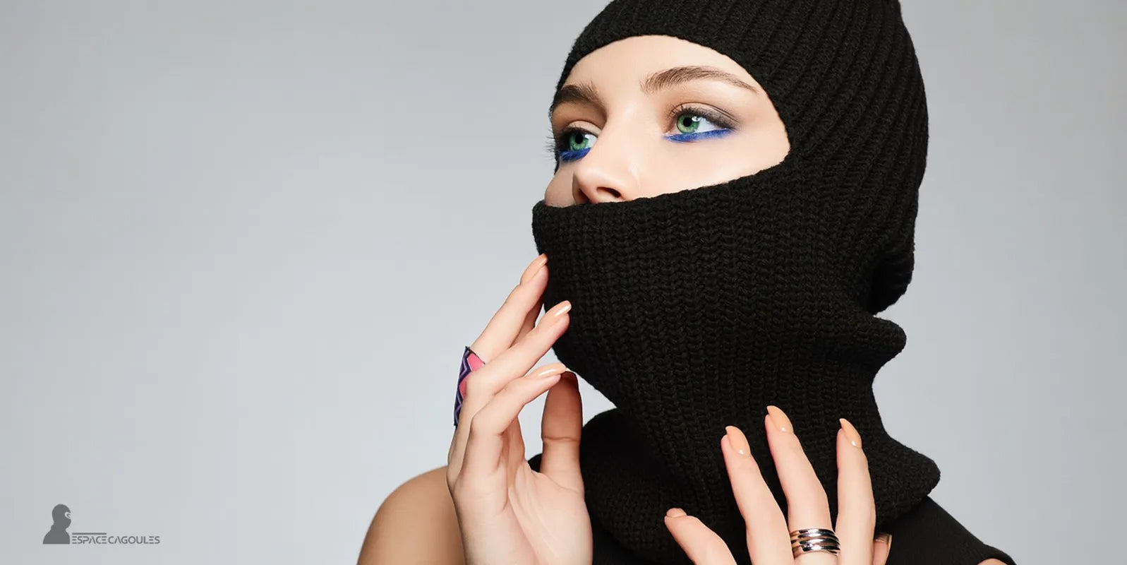 Cagoule Noire femme en maille élégante couvrant le visage jusqu’au nez, avec maquillage bleu et fond gris clair – photographie artistique Espace Cagoules