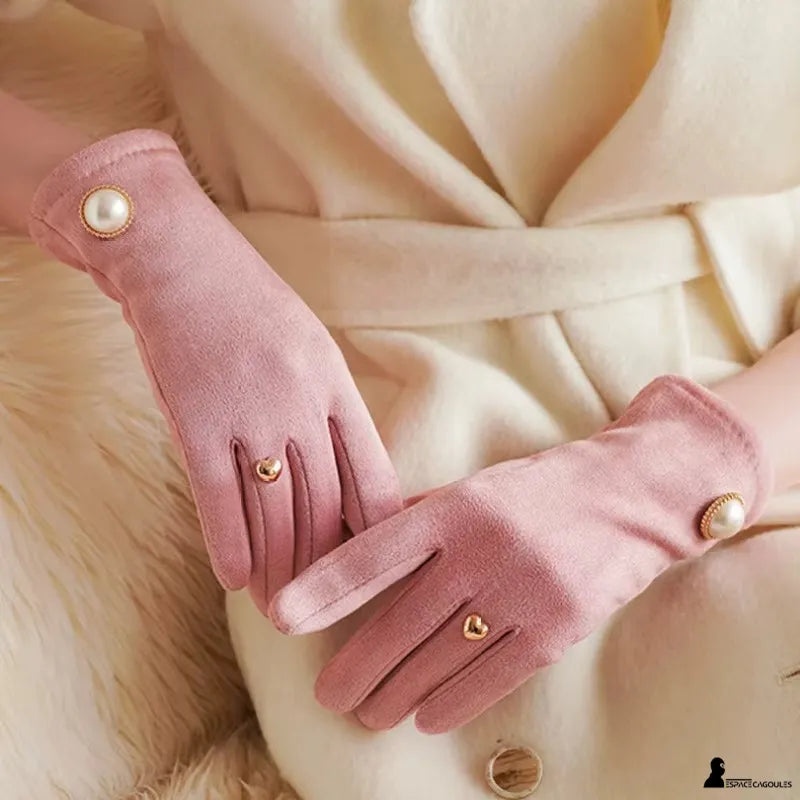 Damen Winterhandschuhe in schickem Rosa, getragen an den Händen, aus Polyester mit samtiger Oberfläche, Fünf-Finger-Form mit Strassdetails und Perlenknopf, getragen in einer winterlichen Innenumgebung - Cagoules Raum.