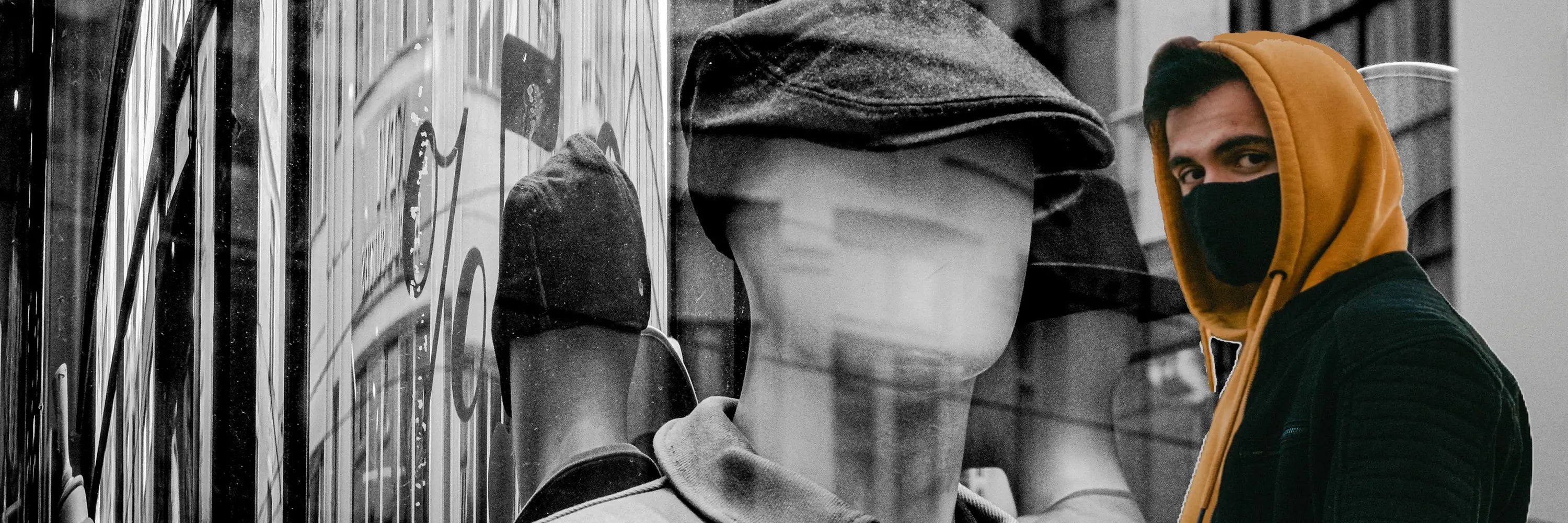 Homme portant un cagoule capuche jaune et un masque noir, observant une vitrine avec des mannequins en arrière-plan dans une scène urbaine.