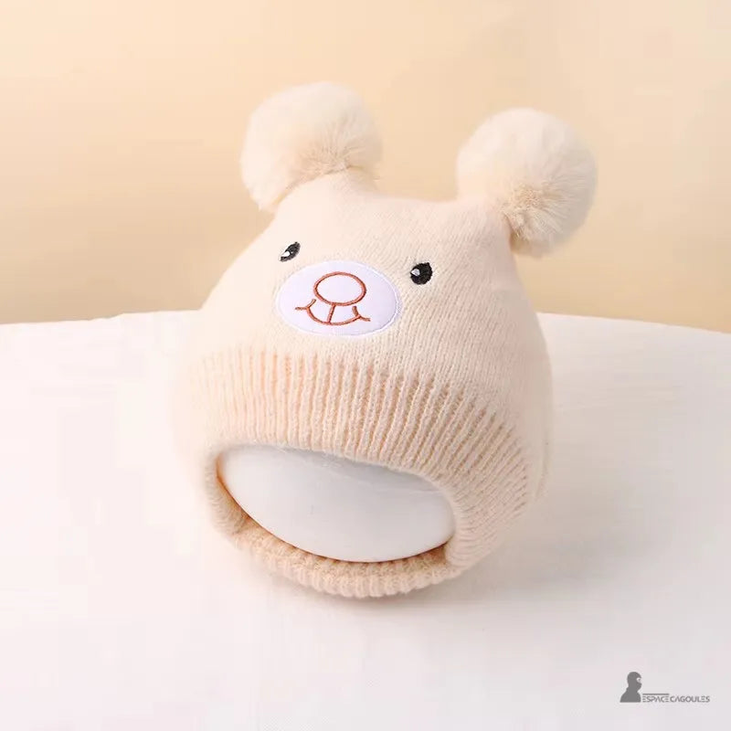 Bonnet Cagoule bébé crème en tricot doux avec oreilles pompons rondes posé sur table claire, accessoire chaud mignon hiver, Espace Cagoules