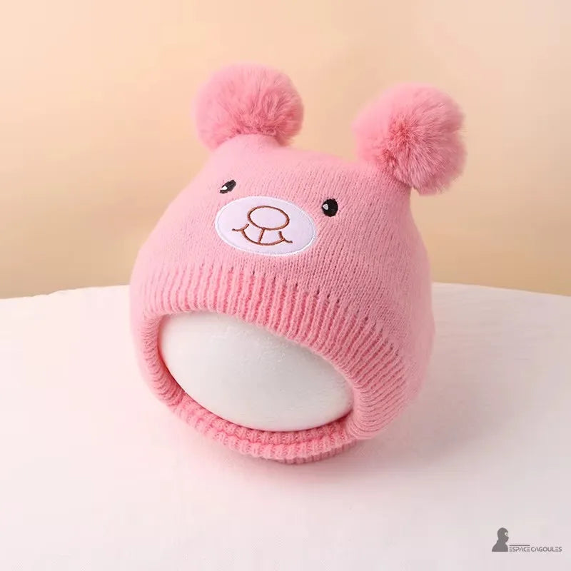 Bonnet Cagoule bébé rose pastel avec oreilles pompons et visage ourson, posé sur table claire pour présentation mignonne, Espace Cagoules