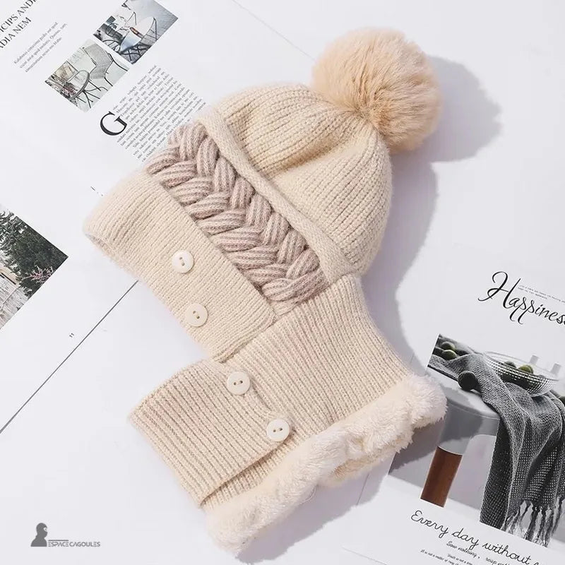 Bonnet cagoule femme beige en laine tricotée avec pompon moelleux et intérieur polaire chaud, posé sur fond clair avec magazine, Espace Cagoules