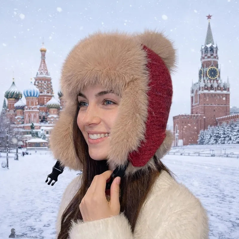 Bonnet chapka fourrure porté par une femme souriante avec bordure épaisse beige et tricot rouge, vue de profil devant la place Rouge enneigée – Espace Cagoules