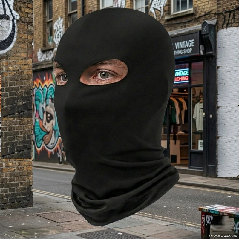 Cagoule 2 trous noire portée en extérieur dans une rue urbaine avec mur en briques et graffiti en arrière-plan, vue trois quarts visage - Espace Cagoules
