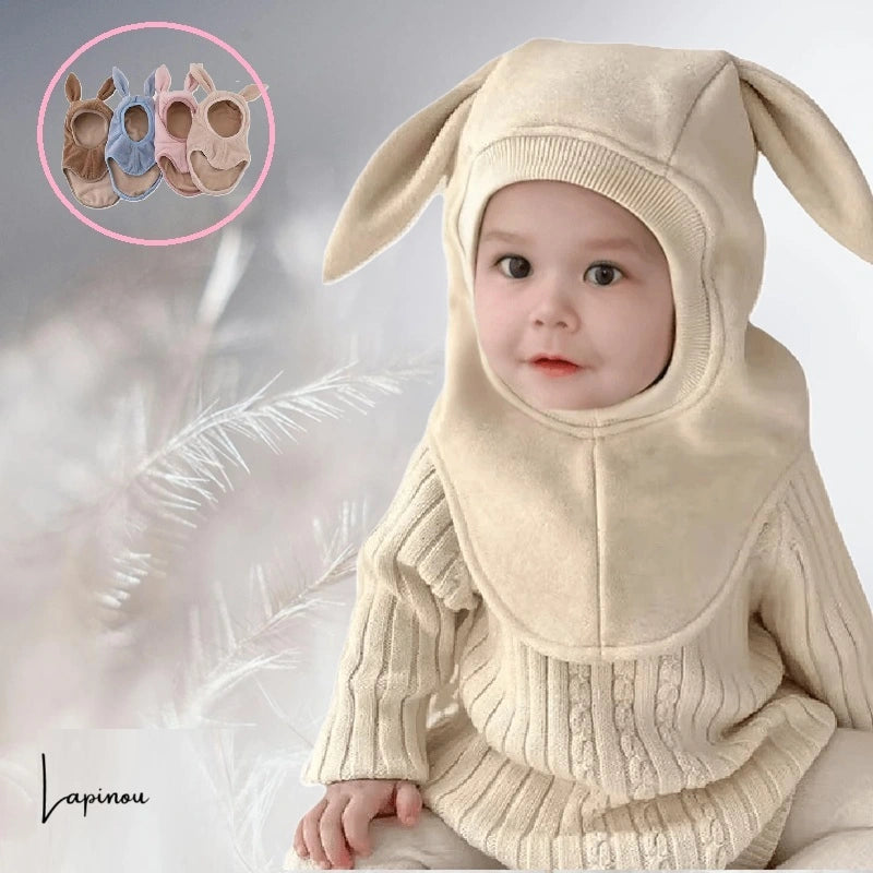 Bébé portant une cagoule bébé polaire beige avec de longues oreilles tombantes, dans un environnement doux et chaleureux. Protection optimale contre le froid.