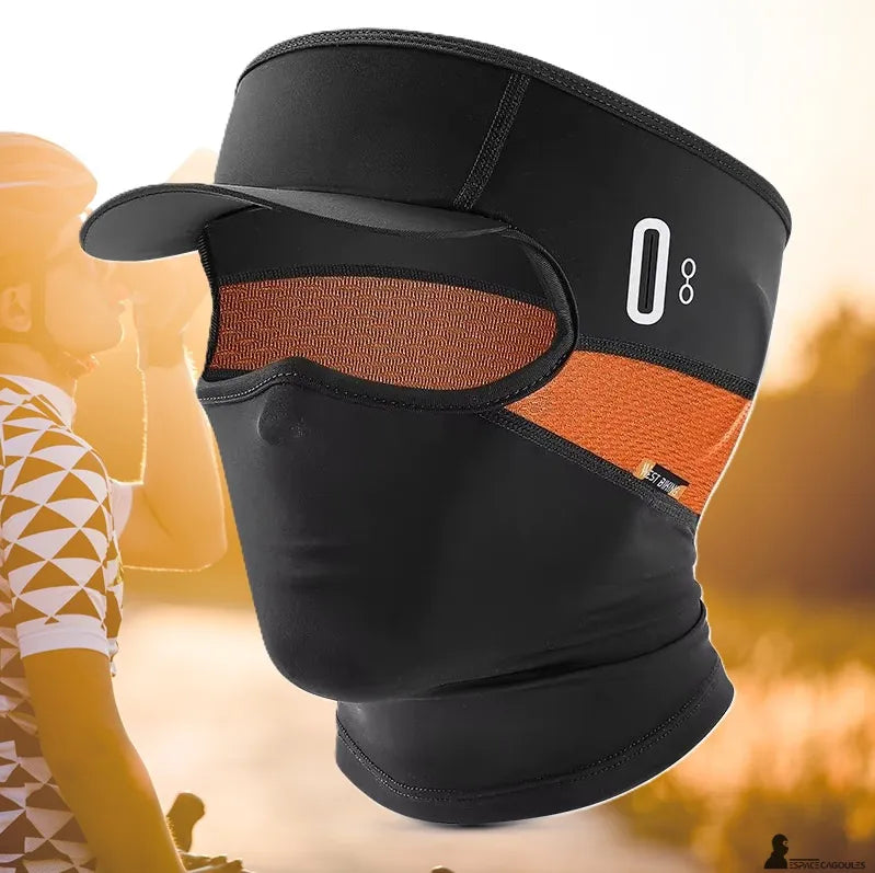 Cagoule casquette vélo été noire avec visière intégrée et panneau latéral orange portée par un cycliste sur route ensoleillée, vue trois quarts profil – Espace Cagoules