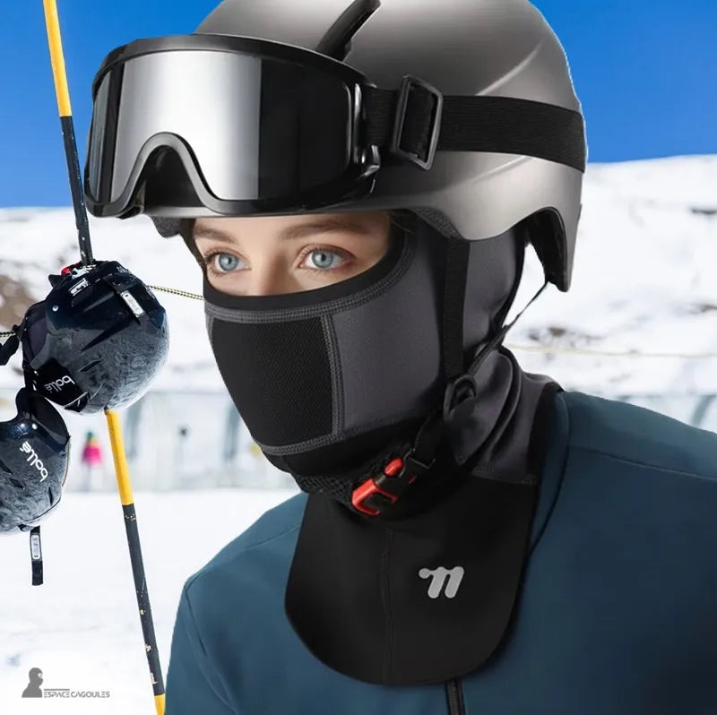 Cagoule de ski à plastron en matière technique respirante, forme intégrale portée par une femme avec casque et masque de ski, vue en situation sur piste enneigée - Espace Cagoules
