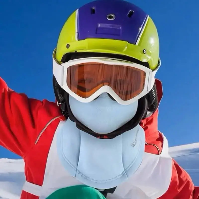 Cagoule de ski enfant SnowKid portée par un enfant avec casque de ski et masque sur une piste enneigée vue de face bras levé – Espace Cagoules