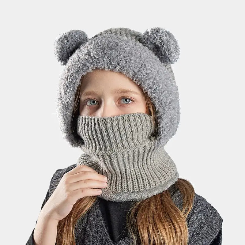 Cagoule enfant fille grise en tricot, avec des oreilles d'ours et un col montant couvrant le visage, portée par une enfant habillée pour l'hiver.