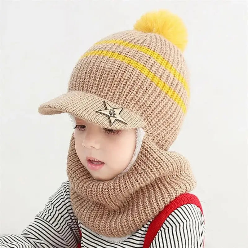 Enfant portant une cagoule enfant tricotée beige avec rayures jaunes, visière étoilée et pompon jaune, couvrant la tête et le cou pour une protection contre le froid hivernal.