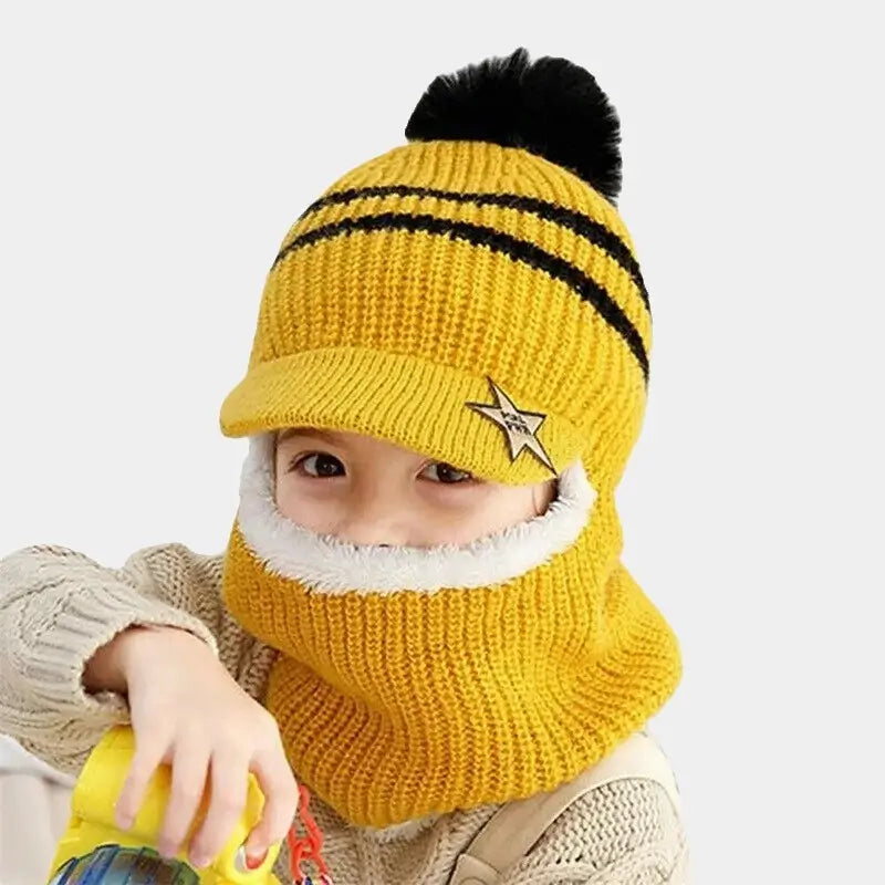 Enfant souriant portant une cagoule enfant tricotée jaune avec rayures noires, visière étoilée et pompon noir, couvrant la tête, le cou et le visage, idéale pour l'hiver.
