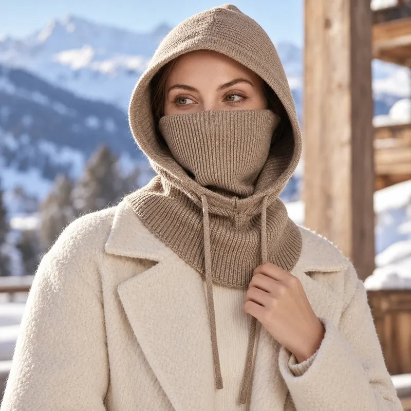 Femme en extérieur enneigé portant une cagoule beige à capuche et col montant remonté sur le nez, devant un paysage de montagne - Espace Cagoules