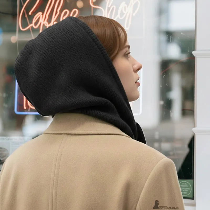 Passamontagna invernale donna nera indossata da una donna di profilo, che cammina davanti a una vetrina di caffè con insegna luminosa, cappuccio ben avvolgente - Spazio Passamontagna