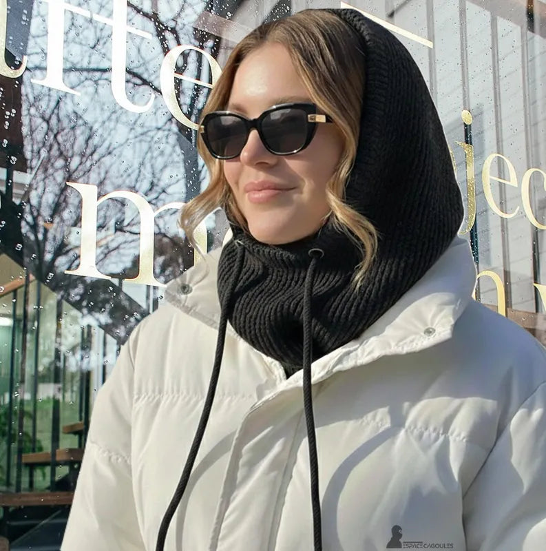 Passamontagna invernale donna nera indossata da una donna bionda con cappotto bianco, in piedi davanti a una vetrina con riflessi di alberi dopo la pioggia, Passamontagna nera aderente che copre testa e collo - Spazio Passamontagna