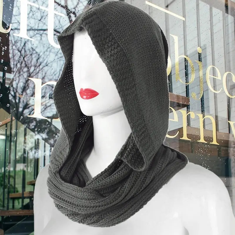 Mannequin portant une cagoule femme en tricot noir avec capuche ample et écharpe intégrée, design moderne et élégant adapté aux tendances mode hivernales.