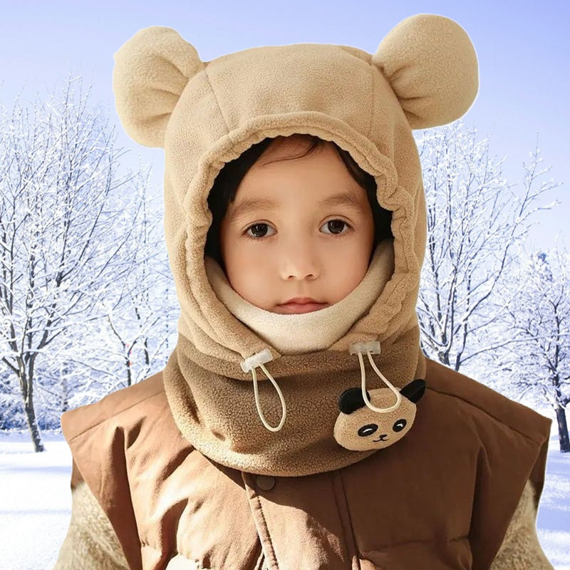 Cagoule grand froid enfant beige avec oreilles d'ours, portée par un enfant souriant en extérieur enneigé, avec cordons ajustables et détails pattes d'ours sur le col.