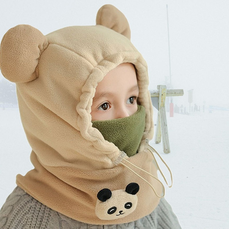 Enfant de profil portant une cagoule grand froid enfant beige avec oreilles d'ours et masque vert couvrant le visage, parfait pour les activités hivernales.