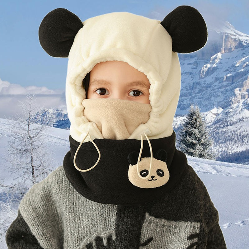 Enfant portant une cagoule grand froid enfant noire et blanche avec oreilles de panda, cache-nez beige et cordons ajustables, sur fond de paysage enneigé avec montagnes et arbres.