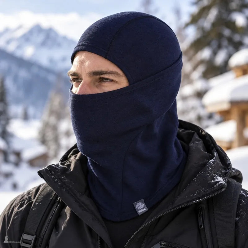 Homme portant la cagoule laine mérinos Ovis bleu roi, masque relevé jusqu'au nez, devant des chalets enneigés - Espace Cagoules