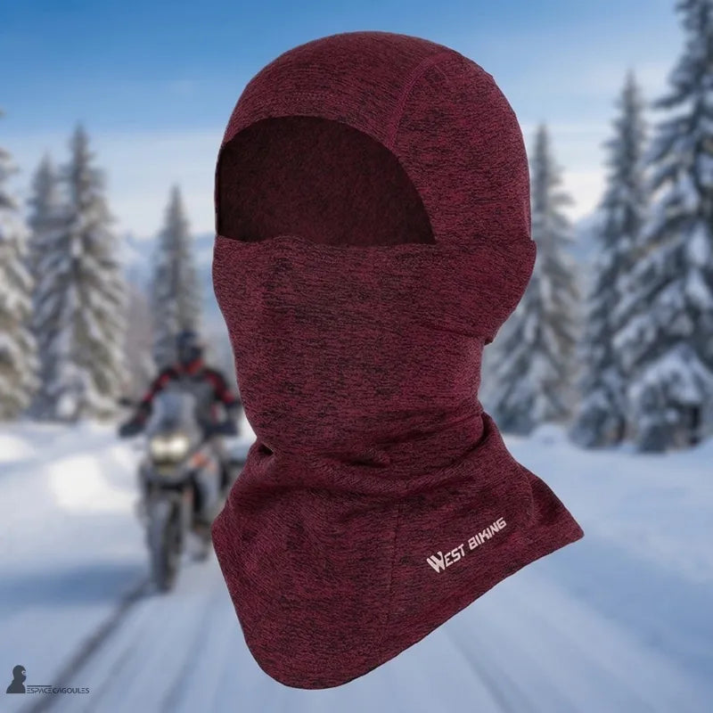 Cagoule moto hiver homme rouge chinée présentée sur mannequin sans visage avec ouverture pour les yeux, décor de forêt enneigée et motard en arrière-plan - Espace Cagoules