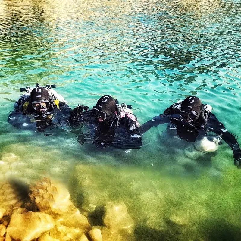 Groupe de plongeurs équipés de combinaisons et de cagoules néoprène thermiques 5 mm, nageant dans une eau turquoise. La cagoule protège efficacement du froid en conditions extrêmes.