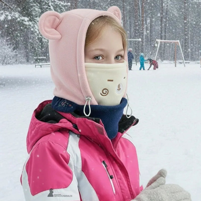 Cagoule polaire enfant 3 à 10 ans - fille en extérieur sous la neige portant cagoule rose et cache-cou crème, ambiance aire de jeu hivernale - Espace Cagoules
