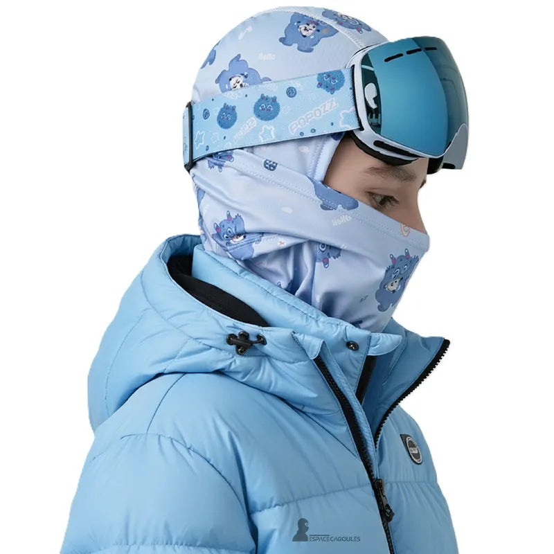 Jeune garçon portant une Cagoule Ski bleue avec casque et masque, protection efficace contre le vent et la neige.
