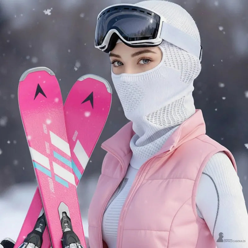 Cagoule ski respirante portée par une femme tenant des skis roses en environnement enneigé avec casque et masque - Espace Cagoules