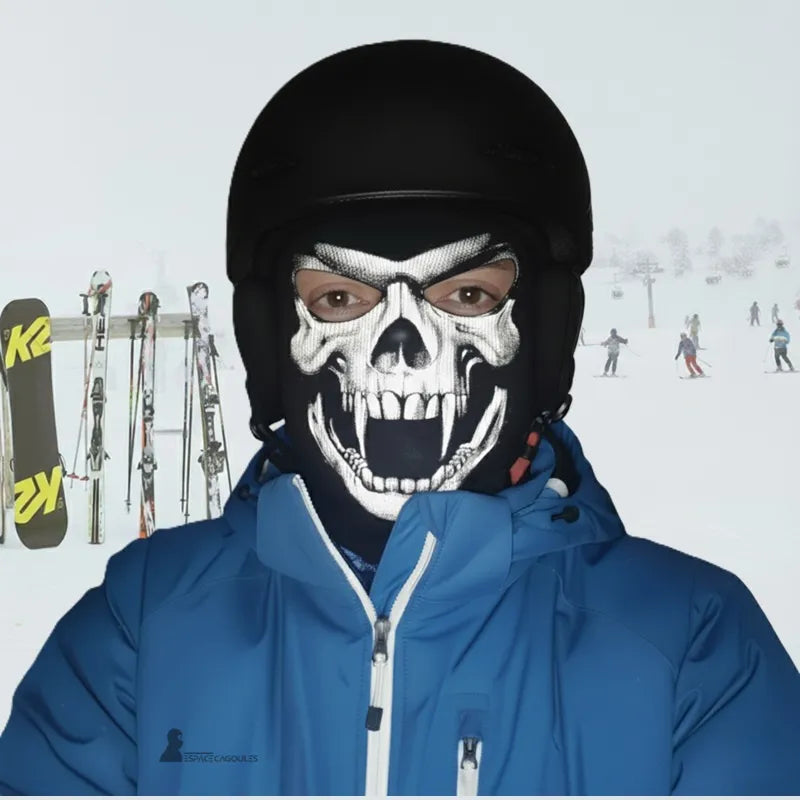 Cagoule ski tête de mort portée sous casque par skieur en veste bleue sur piste de ski, masque tête de mort agressif, Espace Cagoules