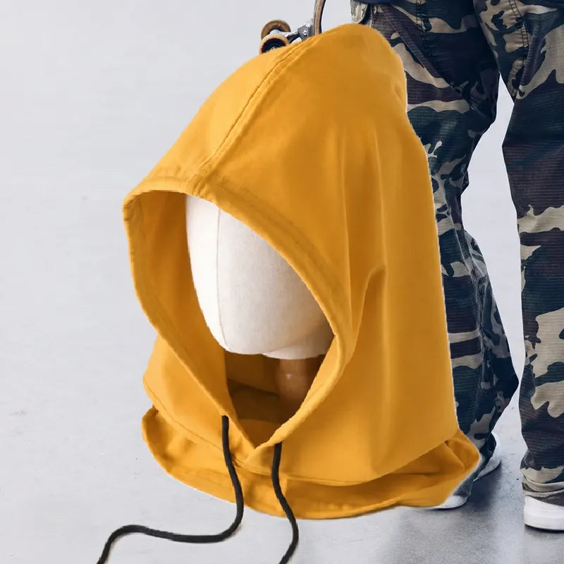Cagoule streetwear jaune moutarde portée dans un décor urbain, à côté d'une personne en pantalon camouflage tenant un skateboard - Espace Cagoules