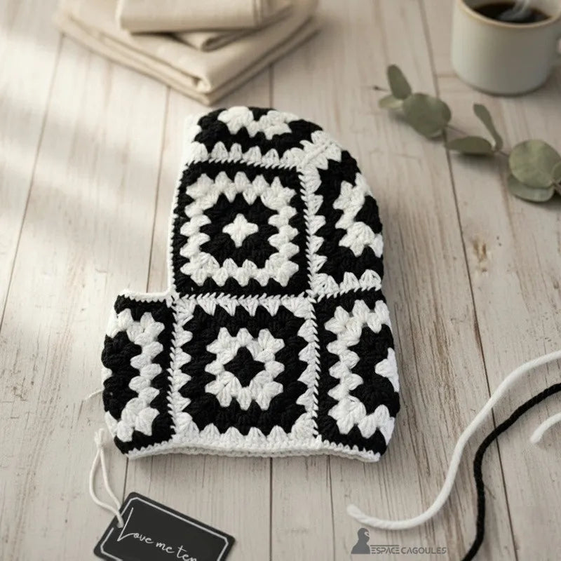 Cagoule tour de cou femme crochet noir et blanc vue de côté posée sur table bois avec accessoire décoratif