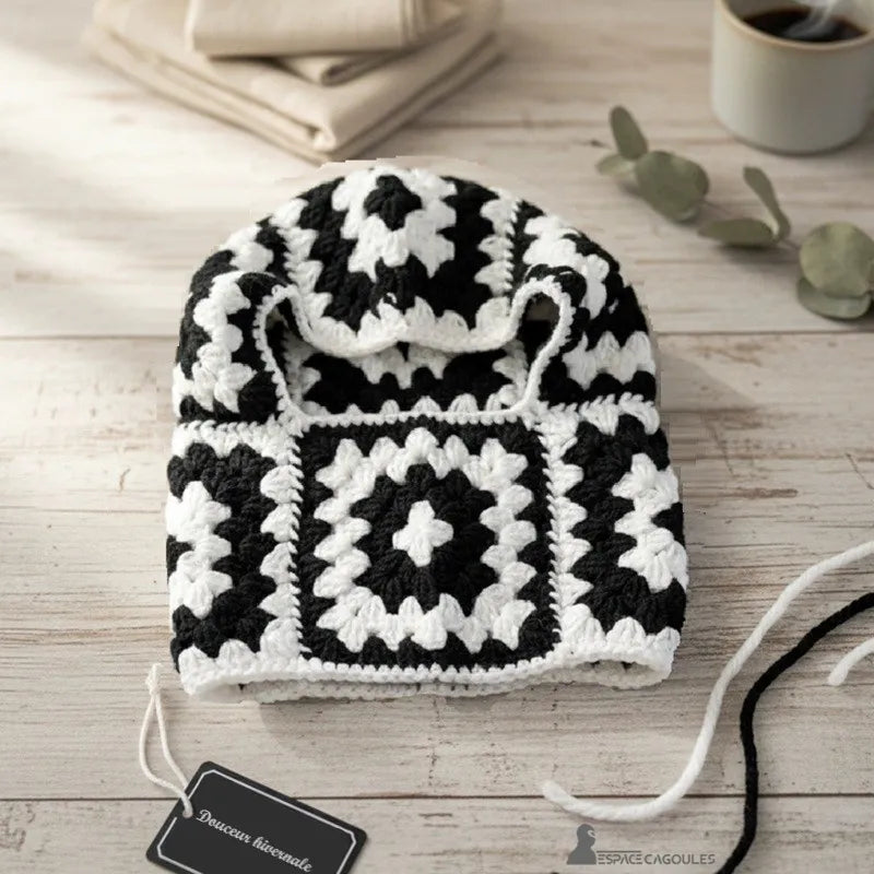 Cagoule tour de cou femme granny square noir et blanc posée sur table en bois avec tasse de café et serviettes