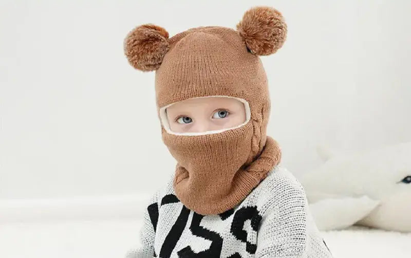 Zoom sur une cagoule tricot enfant coffee avec des pompons façon oreilles d'ourson. La cagoule protège bien le visage tout en laissant un espace pour les yeux.
