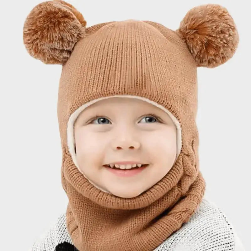 Enfant portant une cagoule tricot enfant coffee avec deux gros pompons en guise d’oreilles. La cagoule couvre toute la tête et le cou, idéale pour l’hiver et les activités en extérieur.