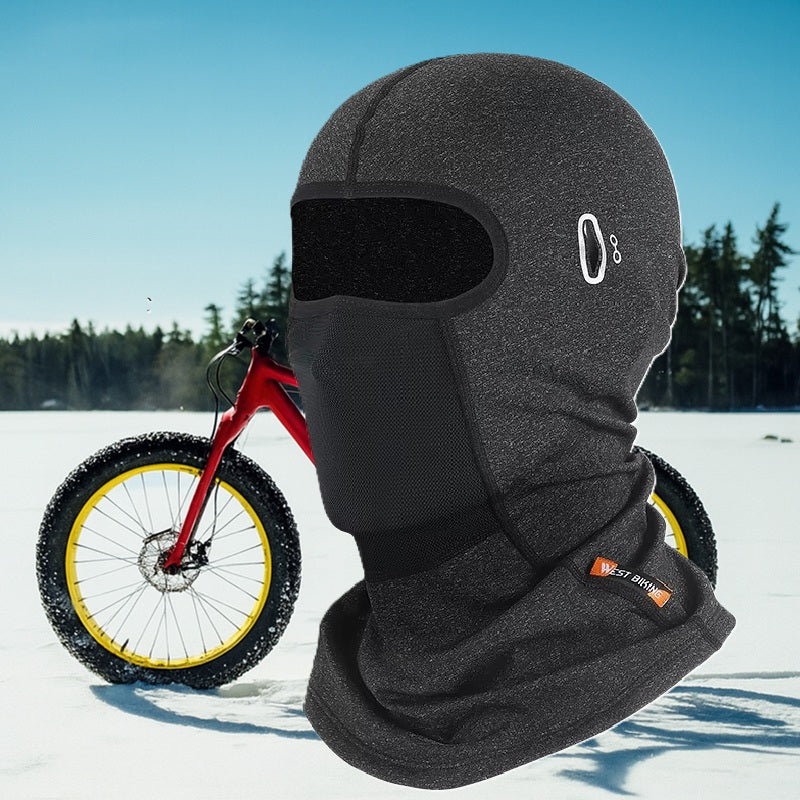 Cagoule vélo hiver grise portée devant un vélo rouge sur neige, adaptée aux environnements froids