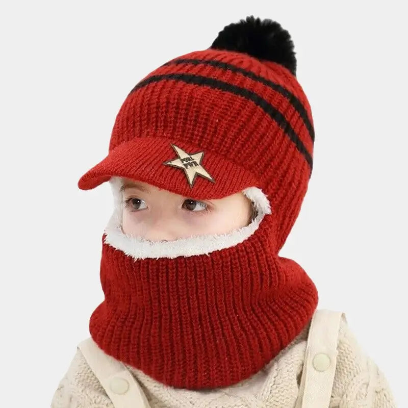 Enfant portant une casquette bonnet enfant tricotée rouge avec rayures noires, visière étoilée et pompon noir, doublure blanche douce, idéale pour protéger du froid en hiver.