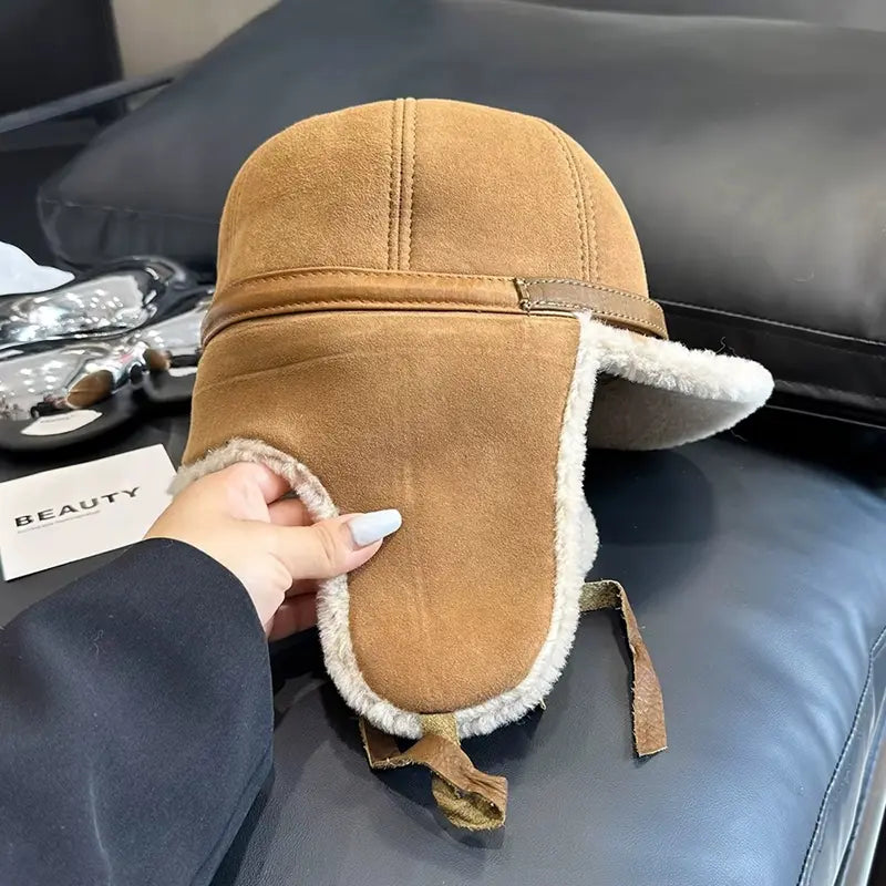 Vue latérale d’une Casquette Chapka beige avec des protège-oreilles en fausse fourrure beige et des cordons d’attache. Une main féminine tient la casquette, mettant en valeur sa coupe ajustée et son style vintage hivernal.