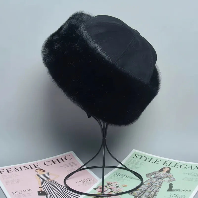 Faux fourrure Chapka in schwarzer Kunstfell und schwarzem Textiloberteil, dicke Chapka-Form, seitliche Ansicht leicht von hinten auf einem Ständer, drinnen vor neutralem Hintergrund - Cagoules Raum.