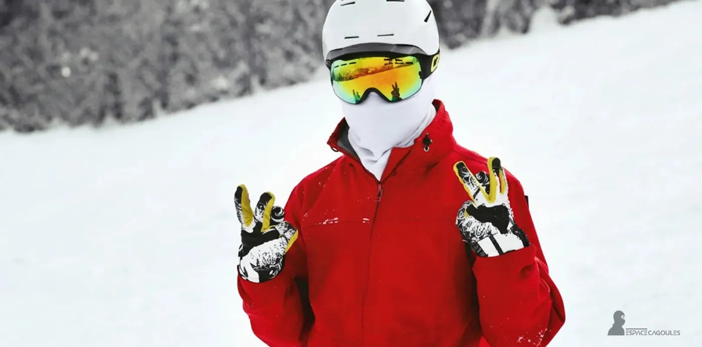 Cagoule blanche de ski ajustée portée sous un casque et des lunettes miroir, skieur en veste rouge sur fond de montagne enneigée levant les mains gantées – Cagoule Blanche Ski - Espace Cagoules