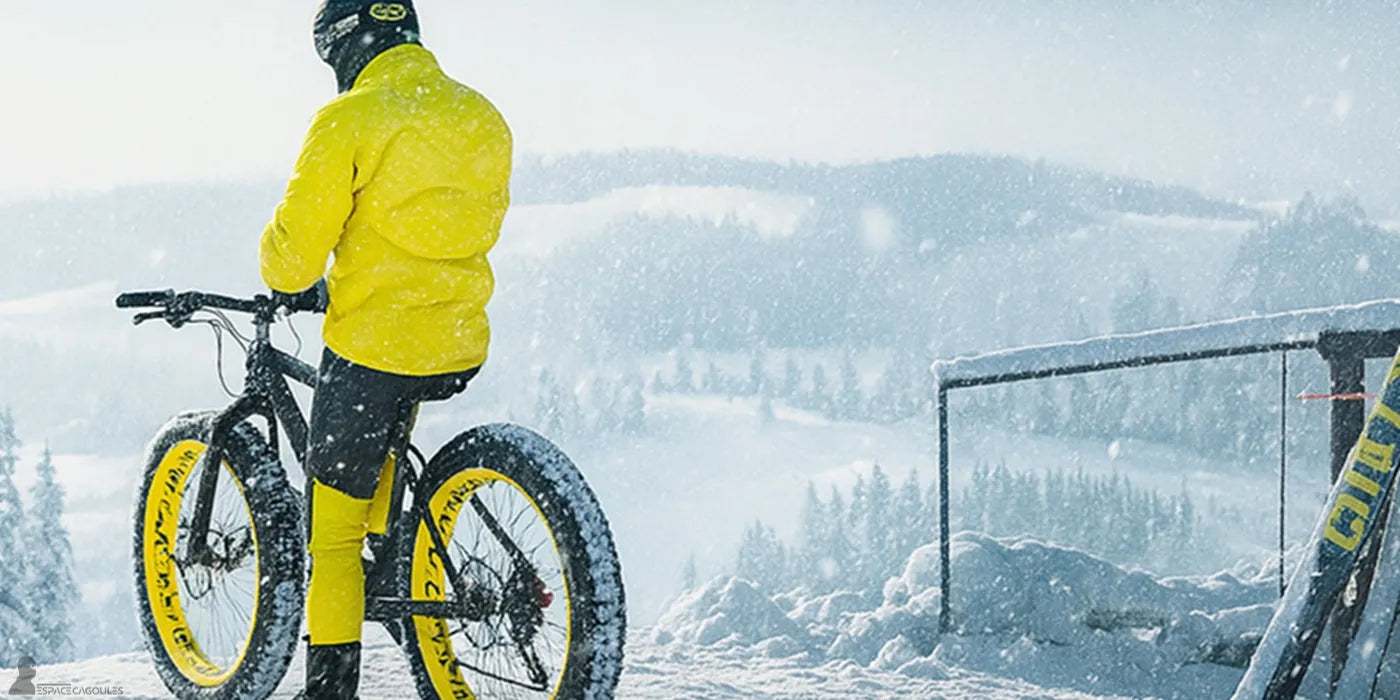 Cycliste en tenue jaune sur vélo à pneus larges dans un paysage enneigé avec visibilité réduite - Espace Cagoules