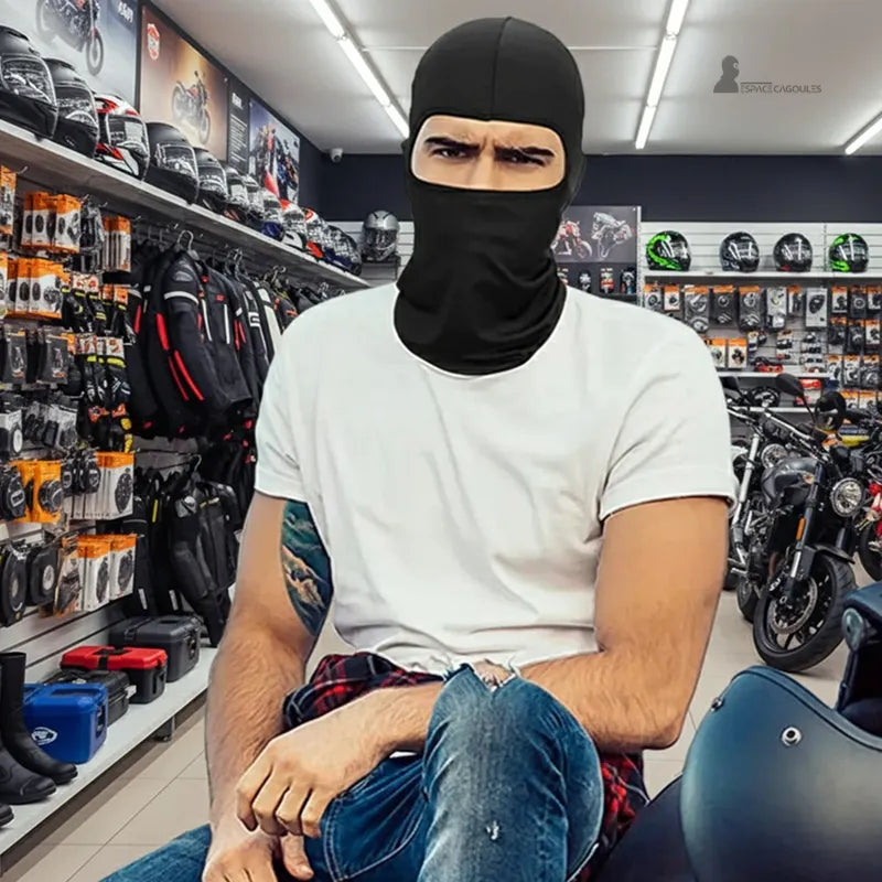 Moto cagoule noire portée par un homme en magasin de moto avec casques et accessoires en arrière-plan