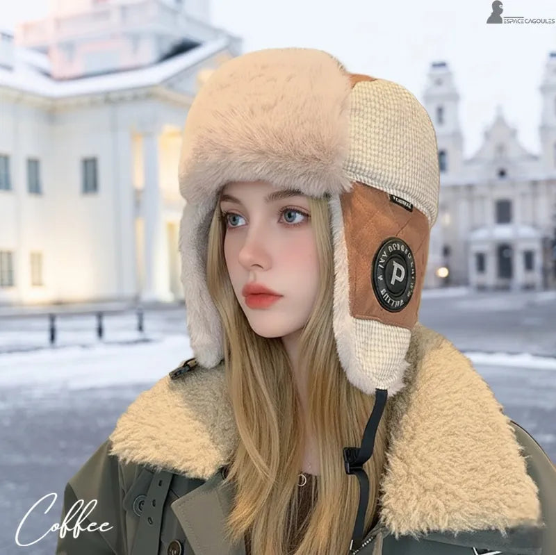 Ouchanka femme portée en extérieur, chapka hivernale en polaire épaisse avec cache-oreilles et design enveloppant, vue trois quarts devant un environnement architectural enneigé - Espace Cagoules