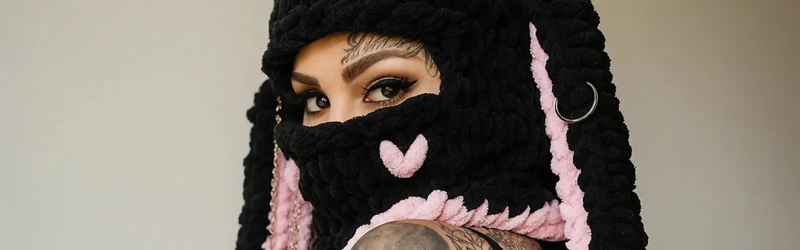 Cagoule originale noire et rose en laine épaisse avec détails cœur, portée par une femme tatouée au regard intense – Collection Cagoules Originales Espace Cagoules