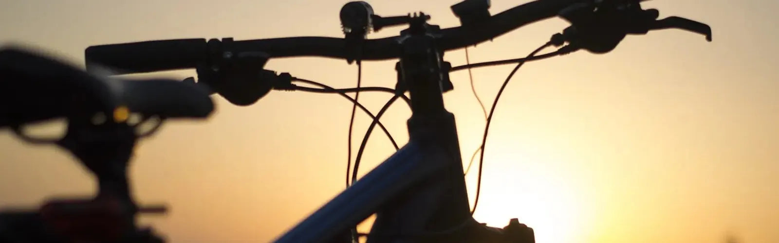 Guidon de vélo en contre-jour sur fond de coucher de soleil, évoquant la collection Cagoules Vélo – Espace Cagoules