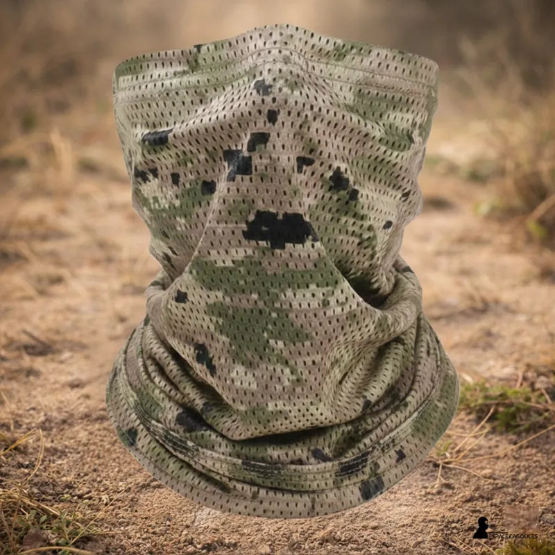 Tour de cou camouflage motif sable posé au sol en extérieur sur un terrain sec, vue de face avec environnement naturel visible - Espace Cagoules